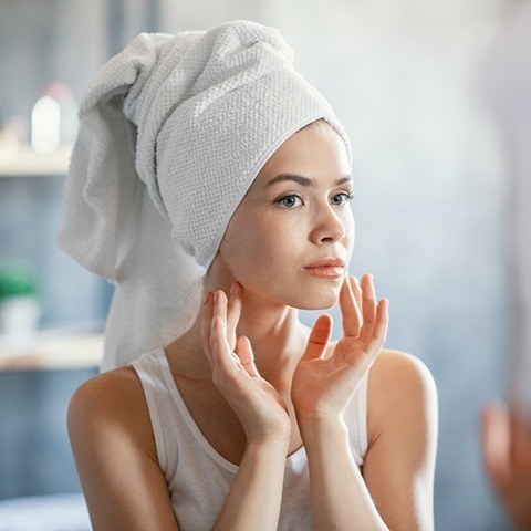 serious lady in bath towel looking at her face in mirror at bathroom
